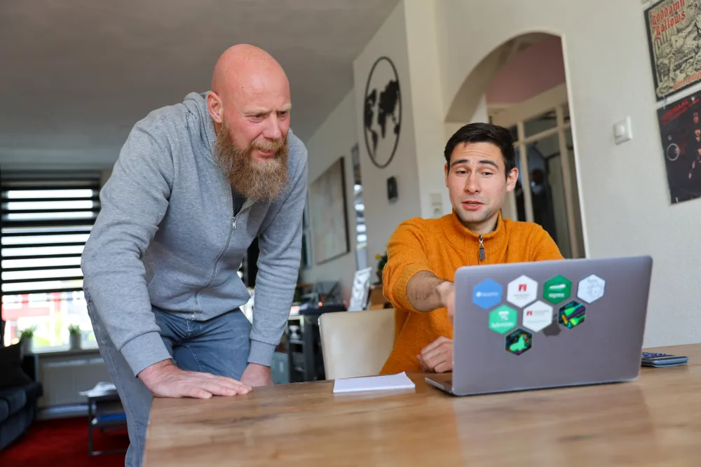 Een oudere host en een jonge huurder kijken samen naar een laptop aan de eettafel