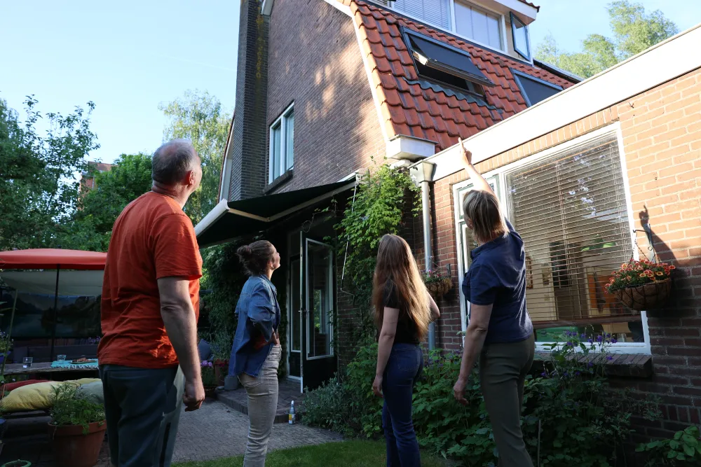 Vier mensen bekijken samen een huis vanuit de tuin tijdens een bezichtiging